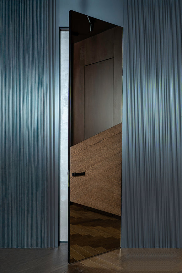 Modern interior door with a reflective surface in a darkly paneled room.